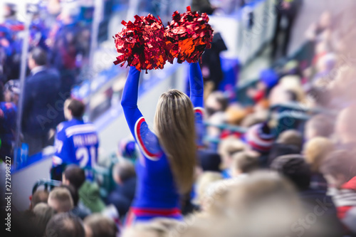 Female cheerleader in red blue uniform with pom-pom with audience in the background performing and supporting during ice hockey game match photo