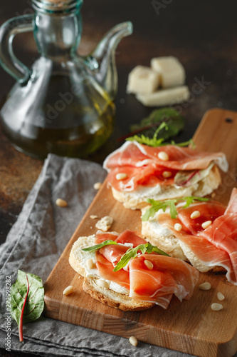 Traditional parma cured ham antipasto. Bruschetta set with Parma Ham and Parmesan Cheese. Small sandwiches with prosciutto, parmesan cheese, fresh arugula, olives and pine nuts