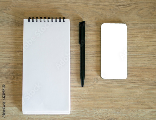 Blank note pad, smartphone and black pen on a wooden table