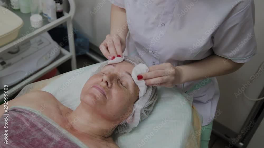 Beautician performs the procedure of washing the face of an elderly woman in a cosmetology clinic. Beautician performs the procedure of washing the face of an elderly woman in a cosmetology clinic.