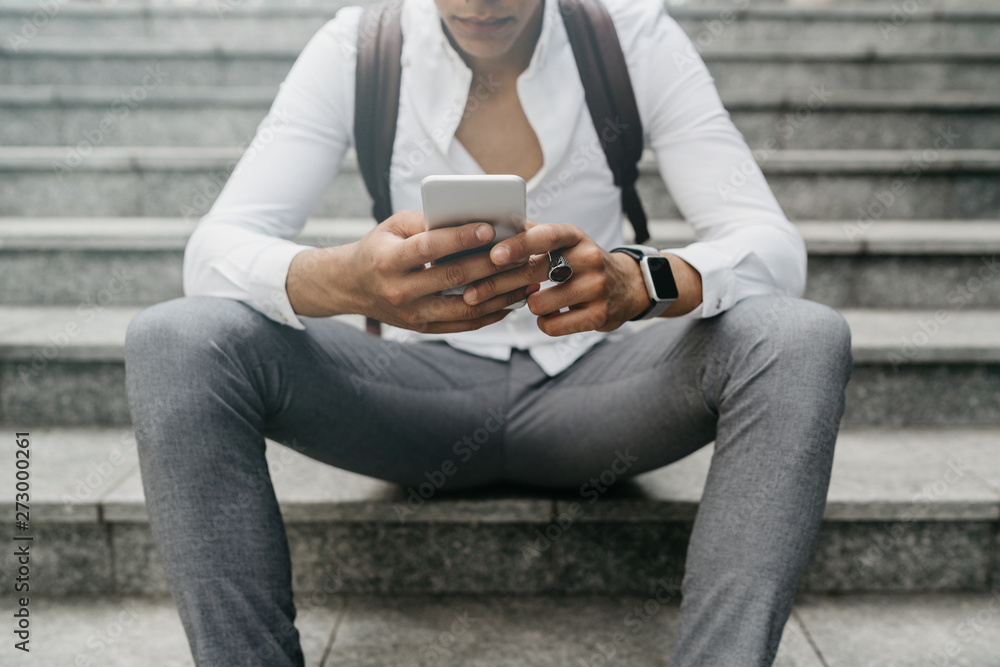 Detail of the hands of a businessman elegantly dressed to sit on the steps of a staircase in a square - Millennial uses the smart phone in a moment of relaxation while surfing on social networks Detail of the hands of a businessman elegantly dressed to sit on the steps of a staircase in a square - Millennial uses the smart phone in a moment of relaxation while surfing on social networks