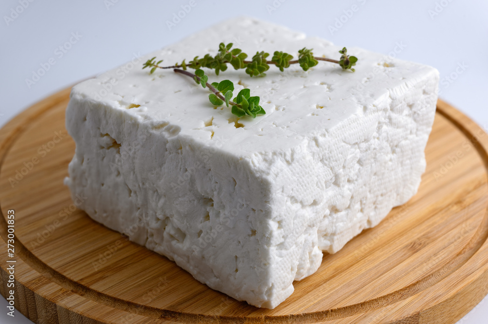 Large piece of traditional greek feta cheese on wooden cutting board with oregano on white background