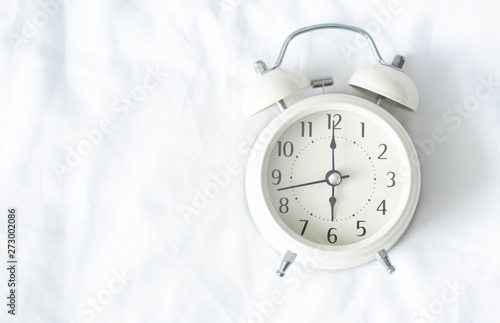 Close up alarm clock on white bed, selective focus