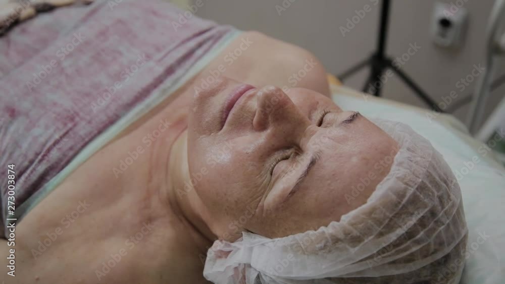 An elderly woman is lying on a couch in a cosmetology clinic. An elderly woman is lying on a couch in a cosmetology clinic.