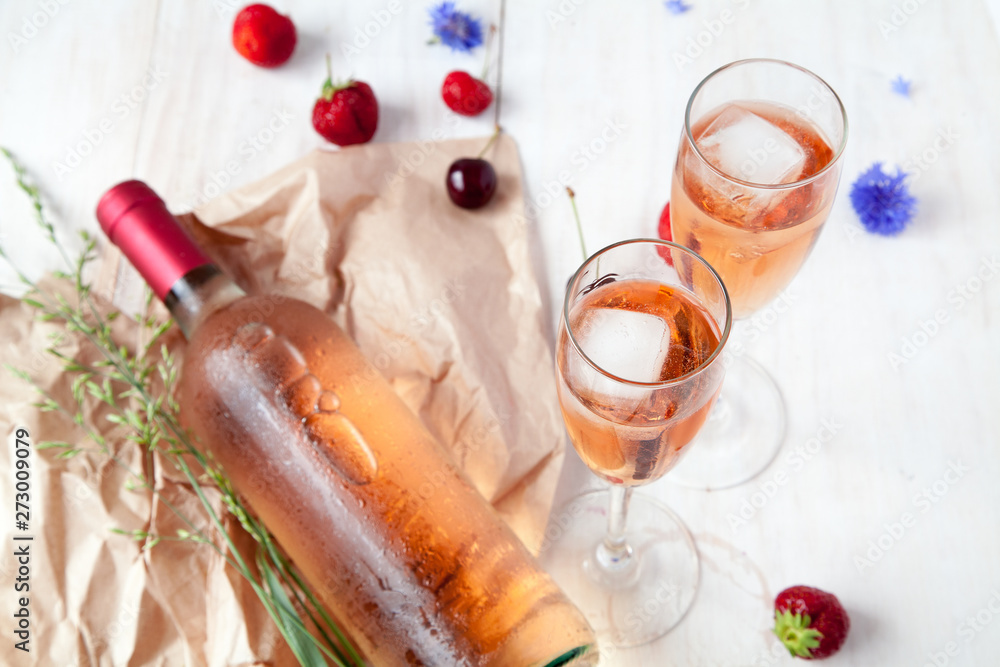 Glasses of rozvogo wine with ice, a bottle of wine, strawberries, cherries and flowers on a white wooden background Glasses of rozvogo wine with ice, a bottle of wine, strawberries, cherries and flowers on a white wooden background