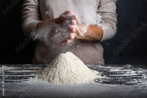 Female hands kneading dough for cooking bread, pizza or pasta. Cook clap hands with flour in the kitchen. Cloud of flour