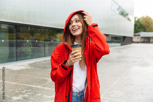 Beautiful excited emotional young happy pretty woman in raincoat posing outdoors drinking coffee.