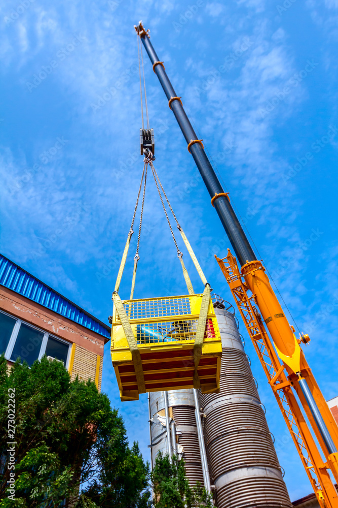 Fototapeta premium Mobile crane with hook and straps is raising work platform, basket