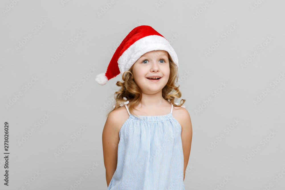 Portrait of a happy smiling little blonde girl on a gray background. Child in santa hat. Christmas celebration concept Portrait of a happy smiling little blonde girl on a gray background. Child in santa hat. Christmas celebration concept