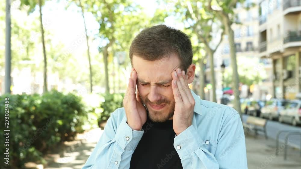 Stressed man complaining suffering migraine in the street Stressed man complaining suffering migraine in the street