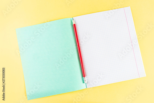 Notebook in a cage and a red pencil with an eraser on a bright yellow background. The concept of the day of knowledge, the first of September. Beginning of the school year.