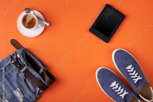 Top view of casual blue suede sneakers with jeans on orange background
