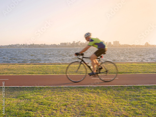 Fototapeta Naklejka Na Ścianę i Meble -  Blurred young man cycling on bike lane along the river