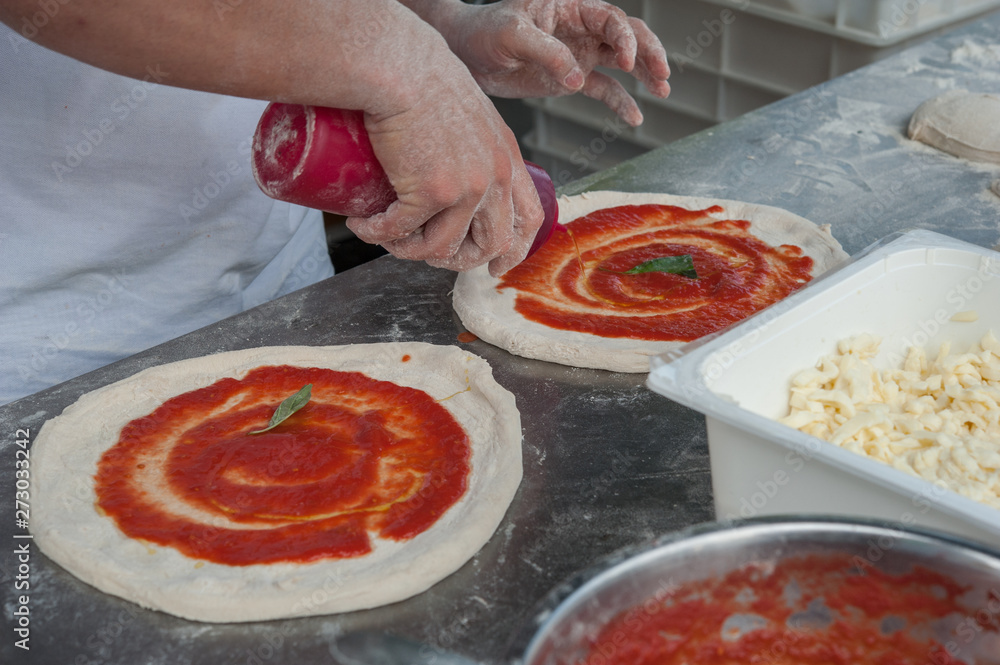 Preparing Pizza Margherita. Pizzaiolo add basil and tomato sauce over a raw pizza dough . Selective focus   
