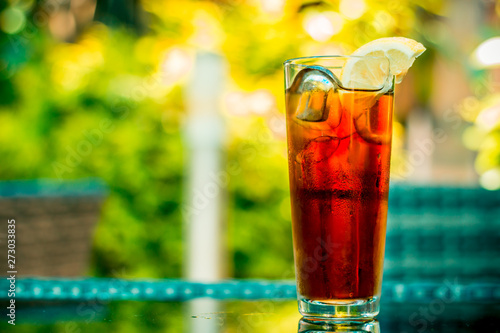 Glass with cold ice tea, cubes and a half slice of lemon on top – Sweet and fruity icy beverage served on hot summer days at bars and restaurants – Refreshing during on colorful background