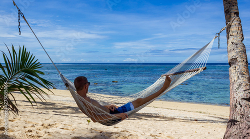 young man enyoing view in a hammock in the shade of palm trees on tropical Fiji Islands