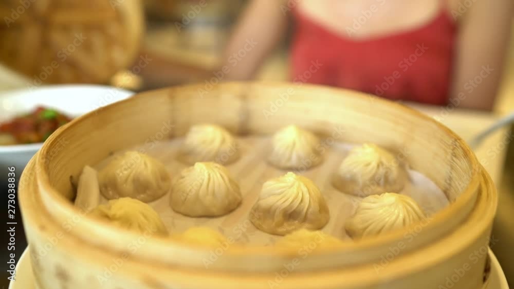 Asian cuisine. Woman eating typical shanghai chinese food xiao long bao soup filled dumplings at restaurant opening bamboo steamer steaming basket tray with hot fresh traditional handmade potstickers.
