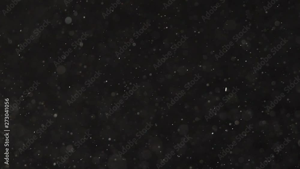Microscopic pieces of dust falling from top to bottom on a black background. Microscopic pieces of dust falling from top to bottom on a black background.