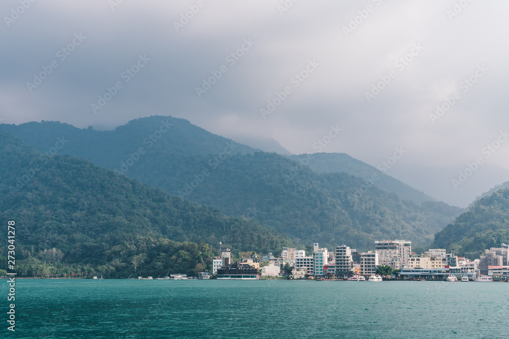 Sun Moon Lake with misty mountain, the Shuishe Pier and buildings in background in Yuchi Township, Nantou County, Taiwan.