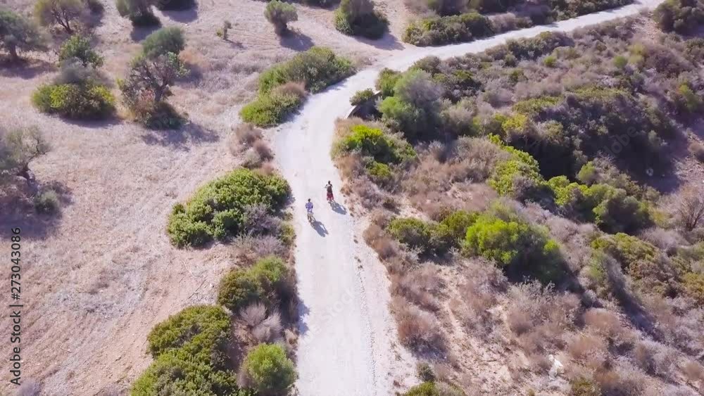 aerial view of two cyclists tourists with child rides on the old asphalt road by bicycle, bushes and farm land, family traveling in Cyprus aerial view of two cyclists tourists with child rides on the old asphalt road by bicycle, bushes and farm land, family traveling in Cyprus