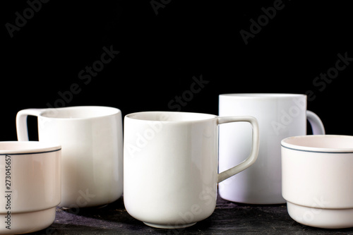 White tea and coffee mugs of various shapes on a wooden table and on a black background.