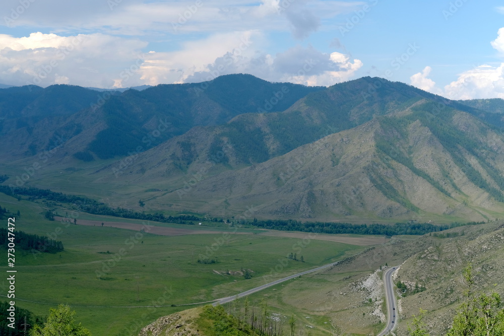 Fototapeta premium Mountain landscape. At the foot of the mountains, plain and the road with cars