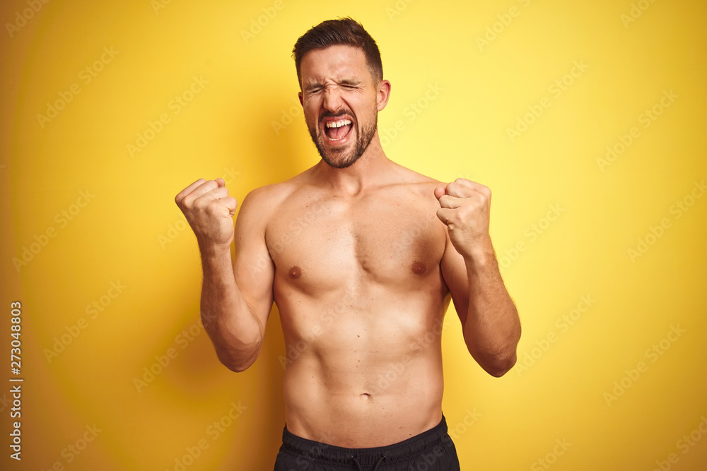 Young handsome shirtless man over isolated yellow background very happy and excited doing winner gesture with arms raised, smiling and screaming for success. Celebration concept.