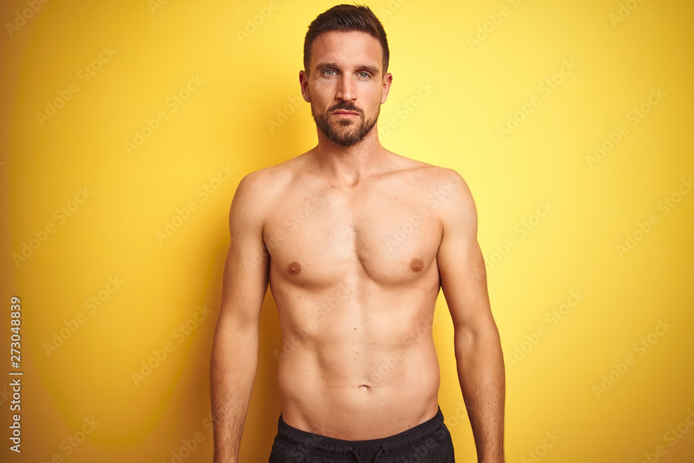 Fototapeta premium Young handsome shirtless man over isolated yellow background with serious expression on face. Simple and natural looking at the camera.