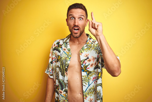 Handsome man wearing summer hawaiian flowers shirt over yellow isolated background pointing finger up with successful idea. Exited and happy. Number one.