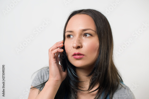 thoughtful young girl talking on the phone and looking away. On light background