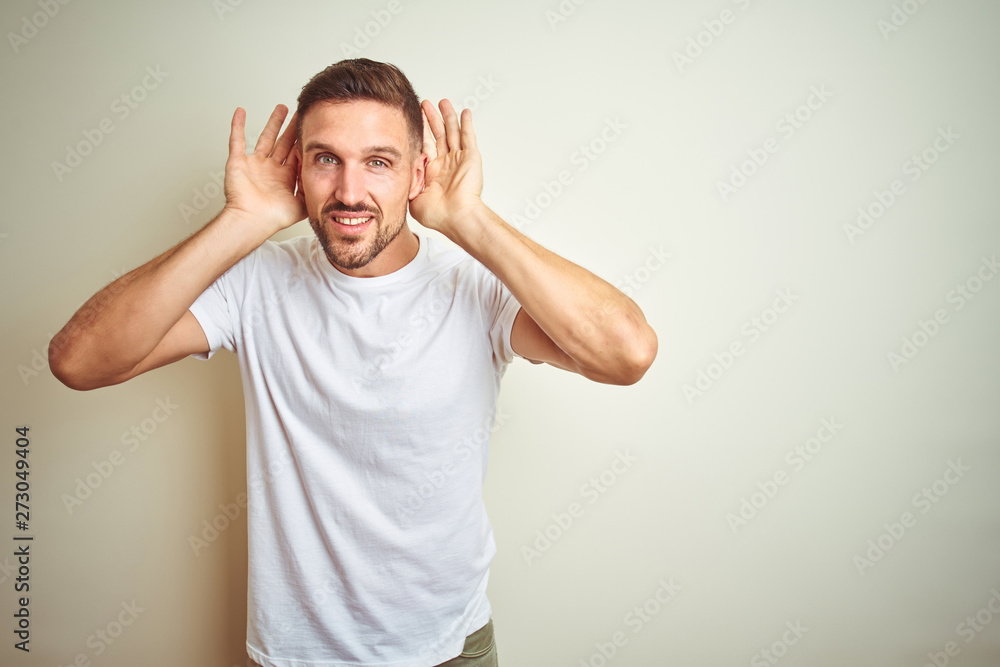 Young handsome man wearing casual white t-shirt over isolated background Trying to hear both hands on ear gesture, curious for gossip. Hearing problem, deaf Young handsome man wearing casual white t-shirt over isolated background Trying to hear both hands on ear gesture, curious for gossip. Hearing problem, deaf