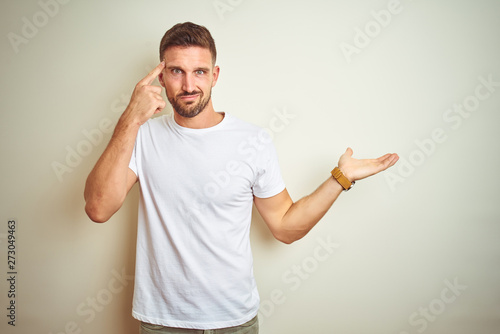 Young handsome man wearing casual white t-shirt over isolated background confused and annoyed with open palm showing copy space and pointing finger to forehead. Think about it.