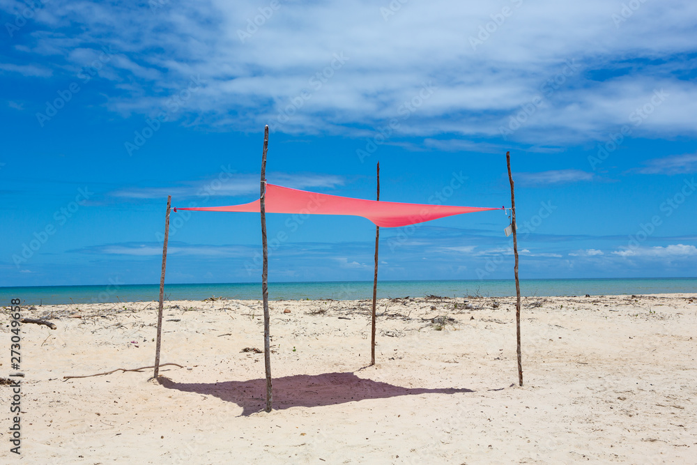 Beautiful beach view with a pink tent on sunny summer day and sea and blue sky in the background. Concept of vacations, peace and relaxation. Ponta do Corumbau, Bahia, Brazil.