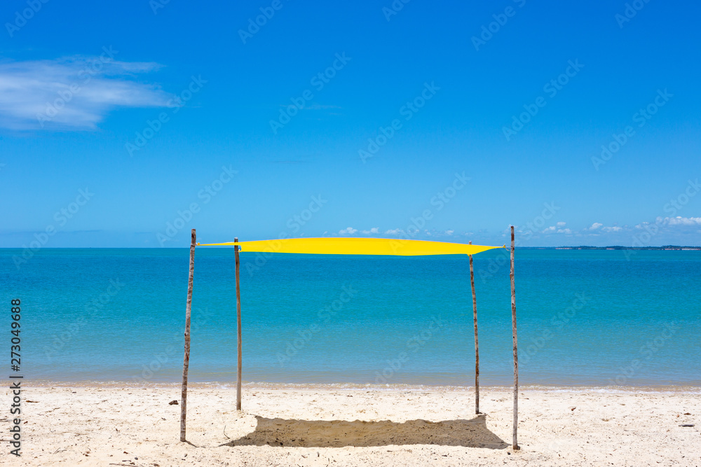 Beautiful beach view with a yellow tent on sunny summer day and sea and blue sky in the background. Concept of vacations, peace and relaxation. Ponta do Corumbau, Bahia, Brazil. Beautiful beach view with a yellow tent on sunny summer day and sea and blue sky in the background. Concept of vacations, peace and relaxation. Ponta do Corumbau, Bahia, Brazil.