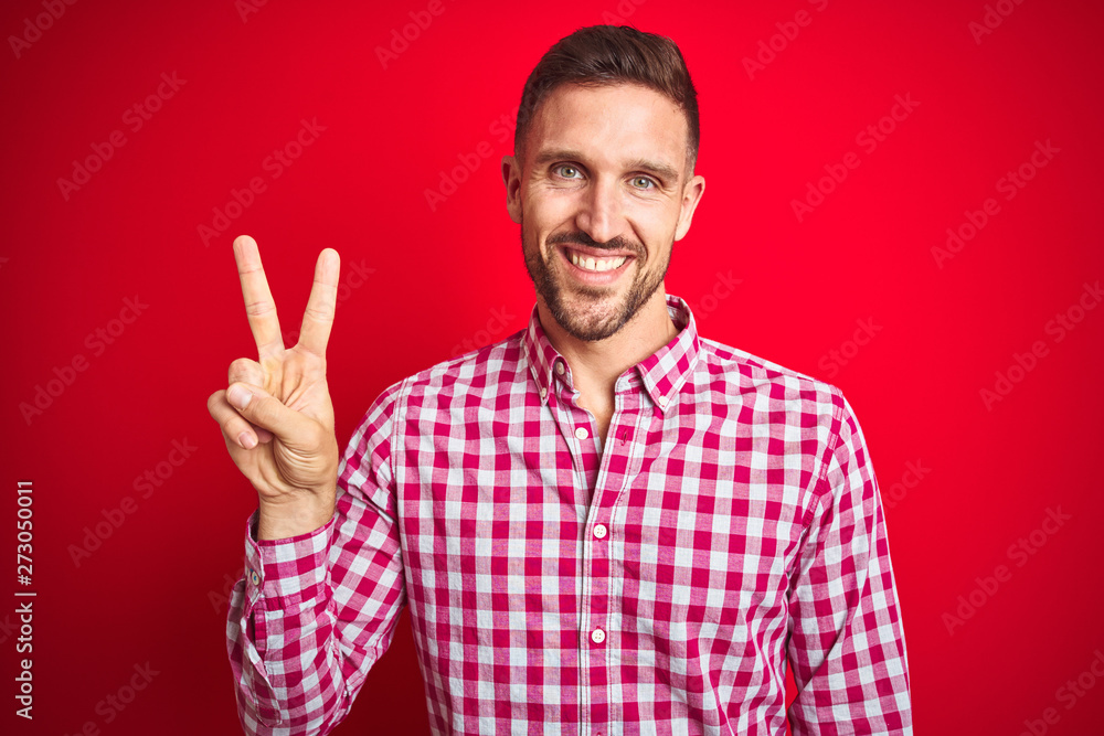 Young handsome man over red isolated background smiling looking to the camera showing fingers doing victory sign. Number two. Young handsome man over red isolated background smiling looking to the camera showing fingers doing victory sign. Number two.