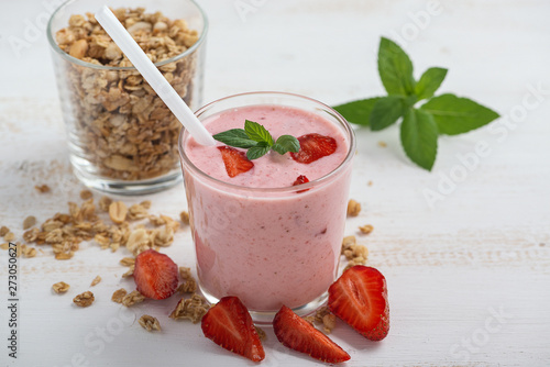 A glass of healthy strawberry yogurt with fresh berries, muesli and mint on a white wooden table. Healthy breakfast.