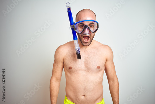 Young man wearing diving snorkel goggles equipent over isolated background afraid and shocked with surprise expression, fear and excited face. photo