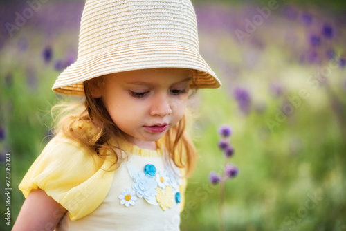 Cute serious baby girl in hat looks down outdoors in green field. Child portrait