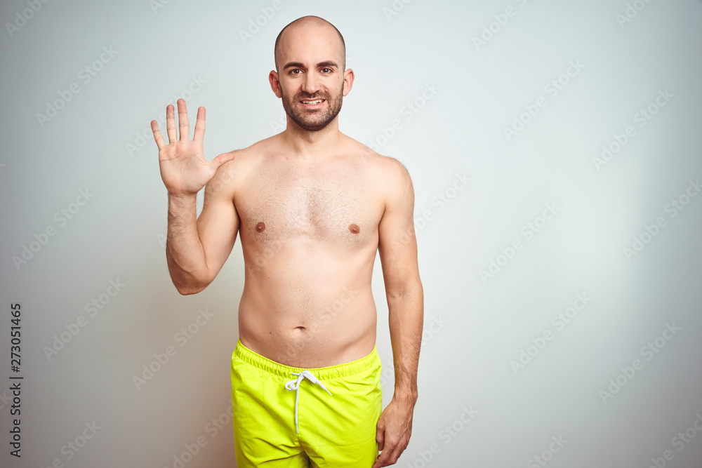 Fototapeta premium Young shirtless man on vacation wearing yellow swimwear over isolated background showing and pointing up with fingers number five while smiling confident and happy.