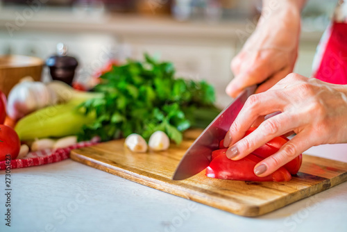 Female hand with knife chops bell pepper in kitchen. Cooking vegetables