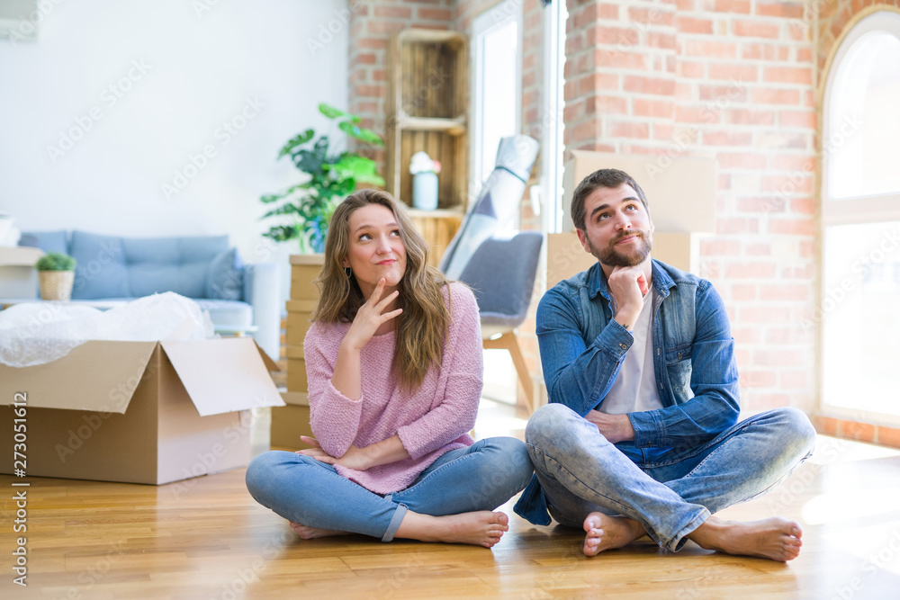 Young beautiful couple moving to a new house sitting on the floor with hand on chin thinking about question, pensive expression. Smiling with thoughtful face. Doubt concept. Young beautiful couple moving to a new house sitting on the floor with hand on chin thinking about question, pensive expression. Smiling with thoughtful face. Doubt concept.