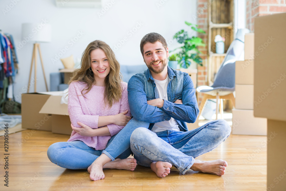 Young beautiful couple moving to a new house sitting on the floor happy face smiling with crossed arms looking at the camera. Positive person. Young beautiful couple moving to a new house sitting on the floor happy face smiling with crossed arms looking at the camera. Positive person.