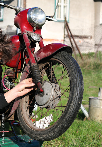 Restoration red old-fashioned motorcycle. Young teenageer repairs rusted wheel and brake malfunction. Typical czech red motorbike in 20th century. Retro style. Fichtl. Fechtl photo