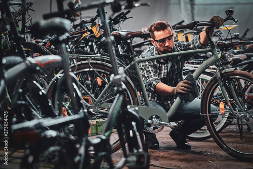 Busy attractive man in protective glasses is cleaning one of bicycle from dust.