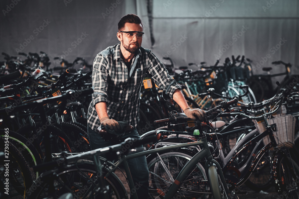 Diligent hardworking man in checkered shirt is working with bicycles at busy warehouse.