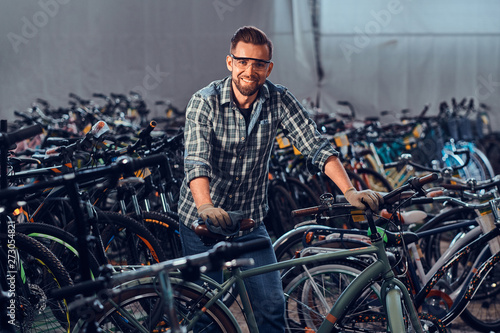 Happy smiling man in protective glasses and shirt is checkin bicycles chain for customer.