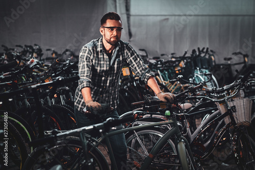 Diligent hardworking man in checkered shirt is working with bicycles at busy warehouse.