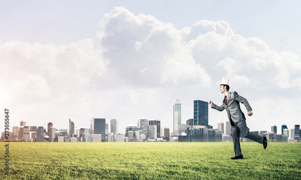 King businessman in elegant suit running on green grass and modern cityscape at background King businessman in elegant suit running on green grass and modern cityscape at background