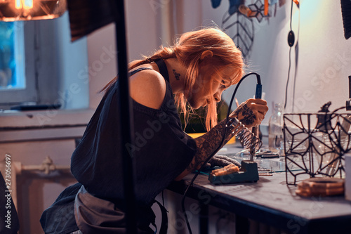 Beautiful diligent woman is doing soldering at her own artisan lamp studio.