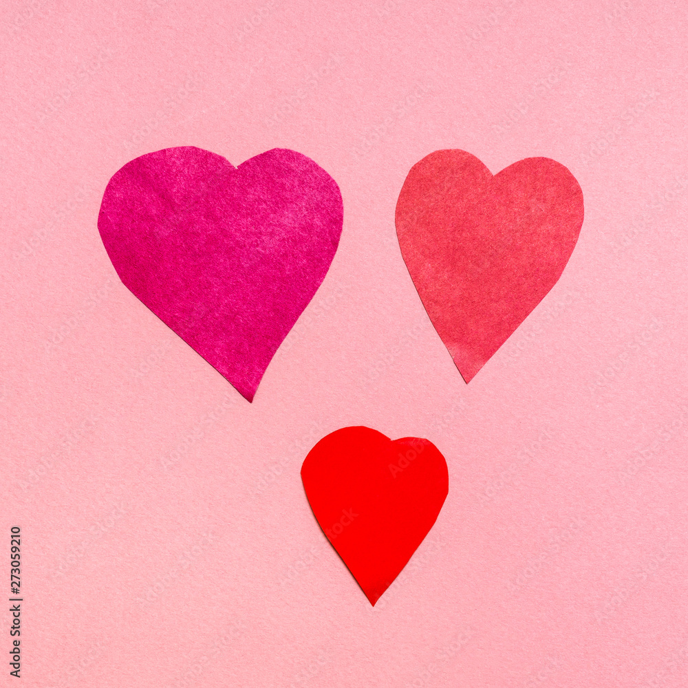 three various hearts cut from red papers on pink